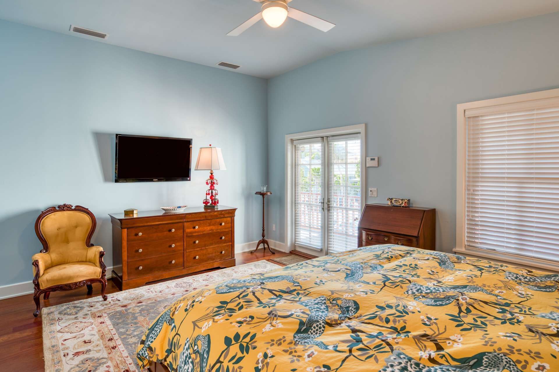 A bedroom with a bed, a dresser, a chair, a television, and a window with blinds.