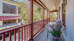 A covered porch with a wooden floor, red railings, and a potted plant.