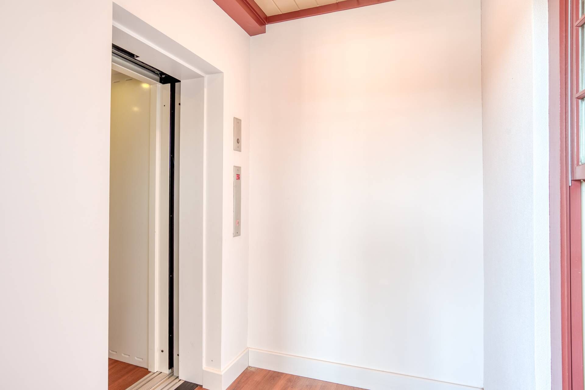 A hallway with a wooden floor, white walls, and a door leading to a room.