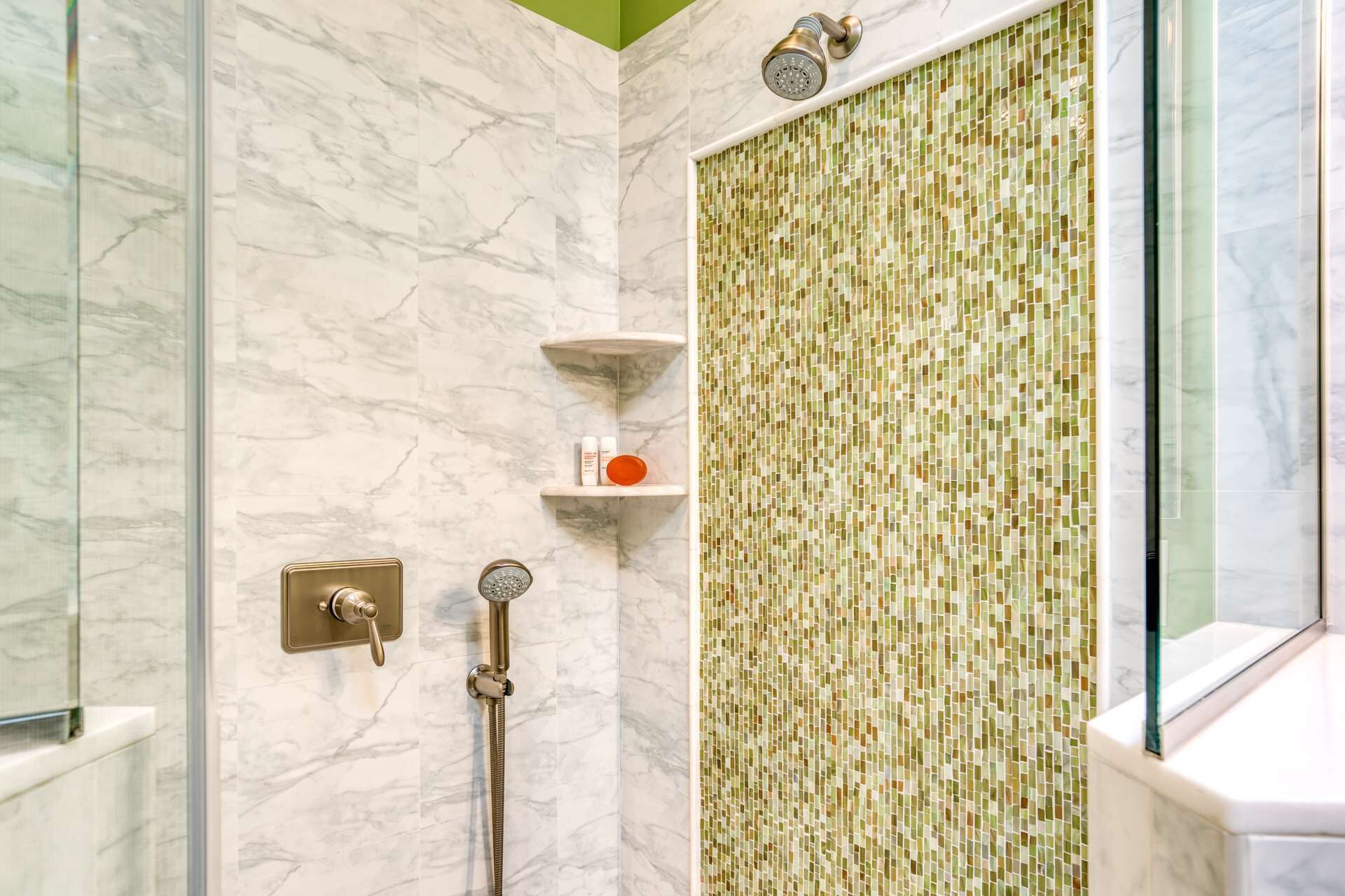 A shower with a mosaic tile wall, marble floor, and a glass enclosure.
