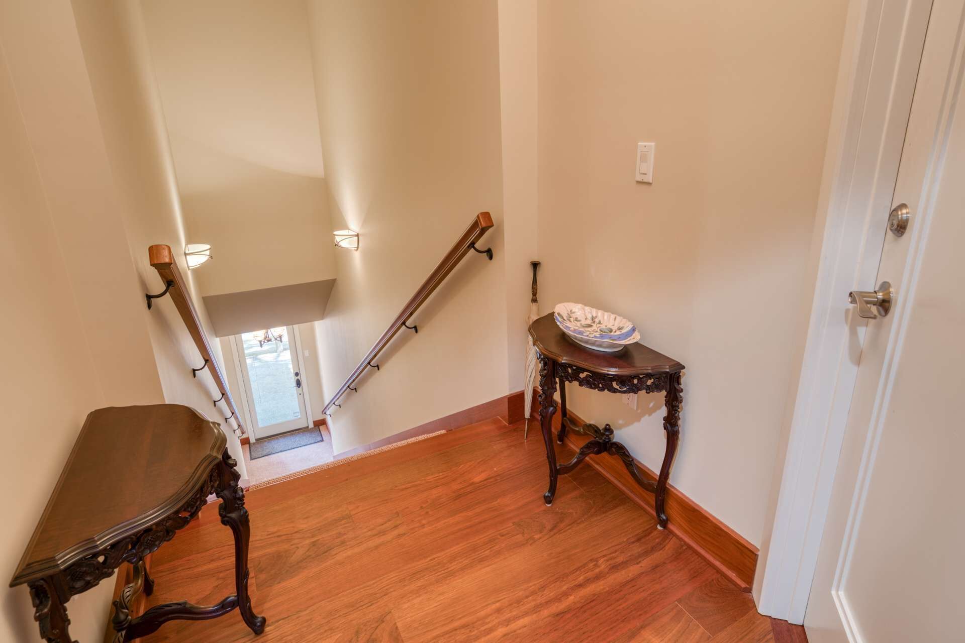A wooden staircase with a handrail, a small table with a bowl on top, and a door with a brass handle.