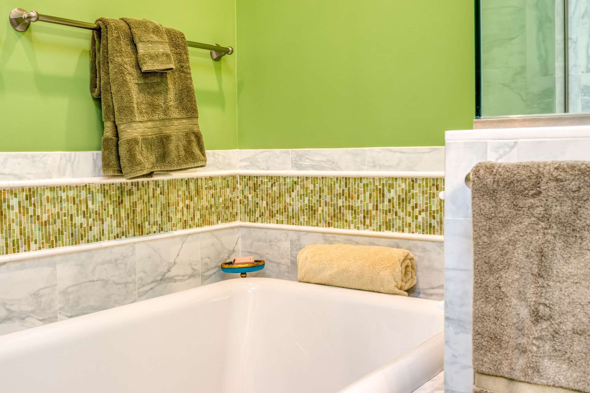 Casa de banho com banheira branca, paredes verdes e uma moldura de azulejos em mosaico.