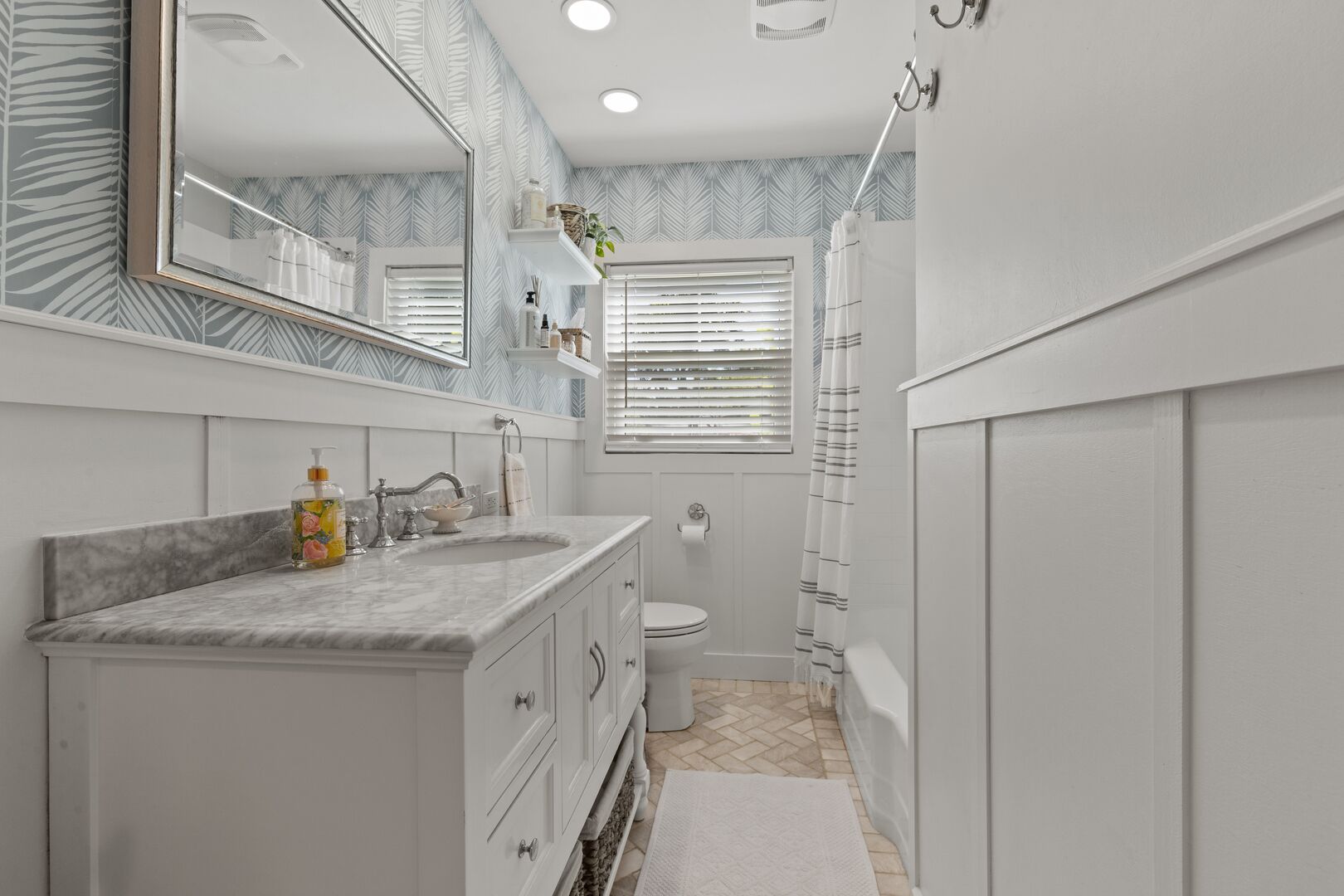 A bathroom with a marble vanity, a large mirror, a toilet, and a shower area.