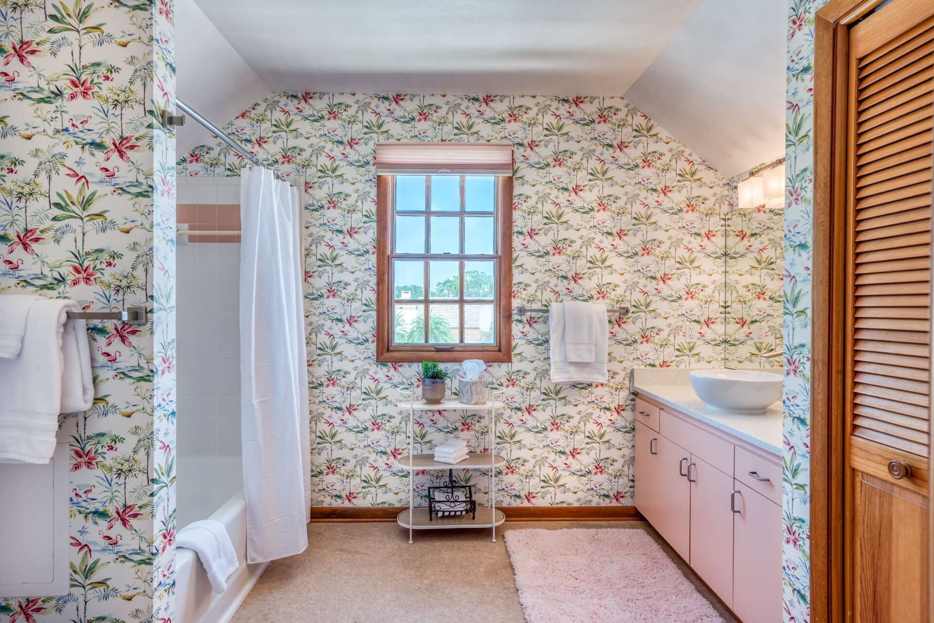 A bathroom with floral wallpaper, a window, a sink, and a shower.