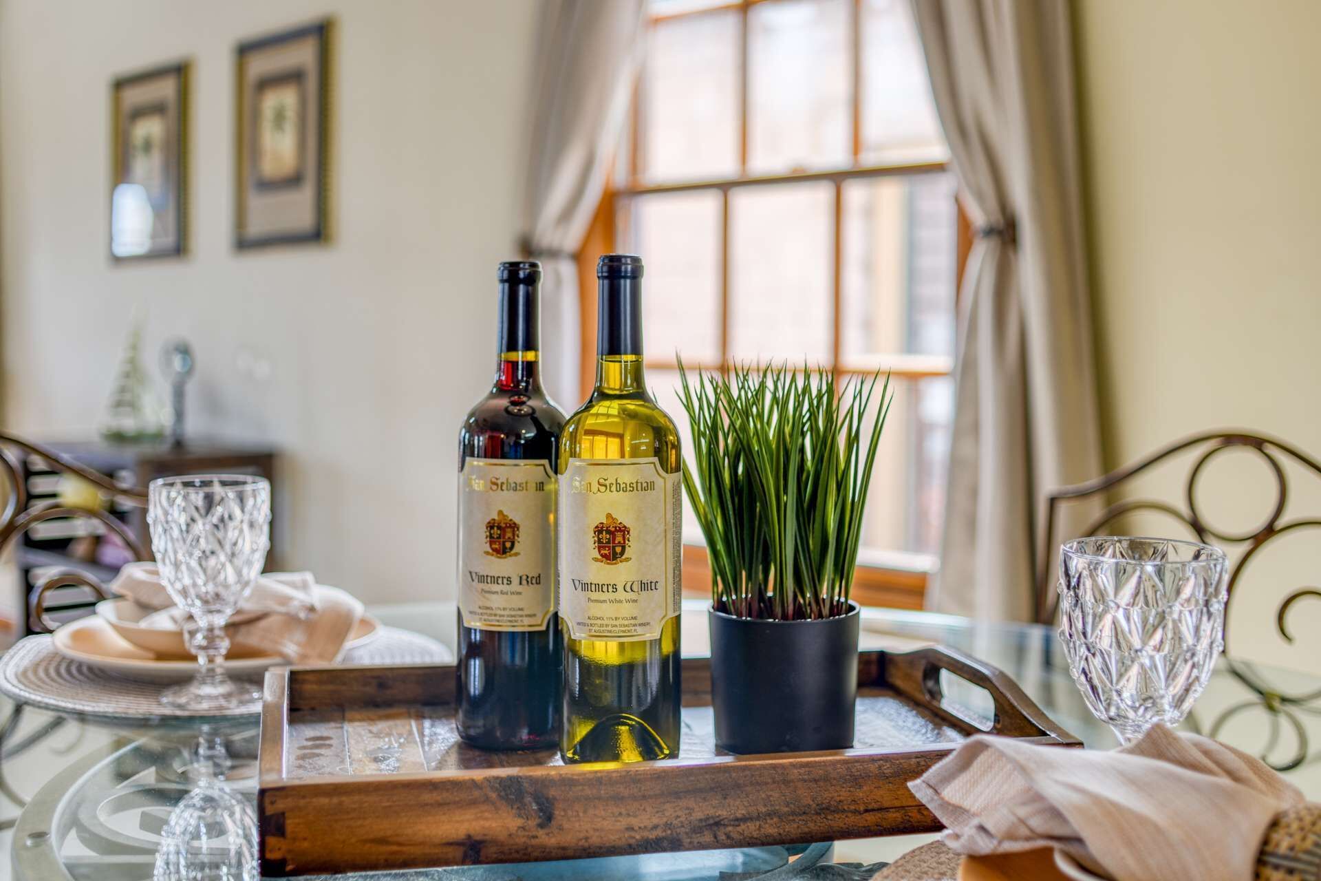 Una mesa de comedor con dos botellas de vino, una copa y una planta en maceta.
