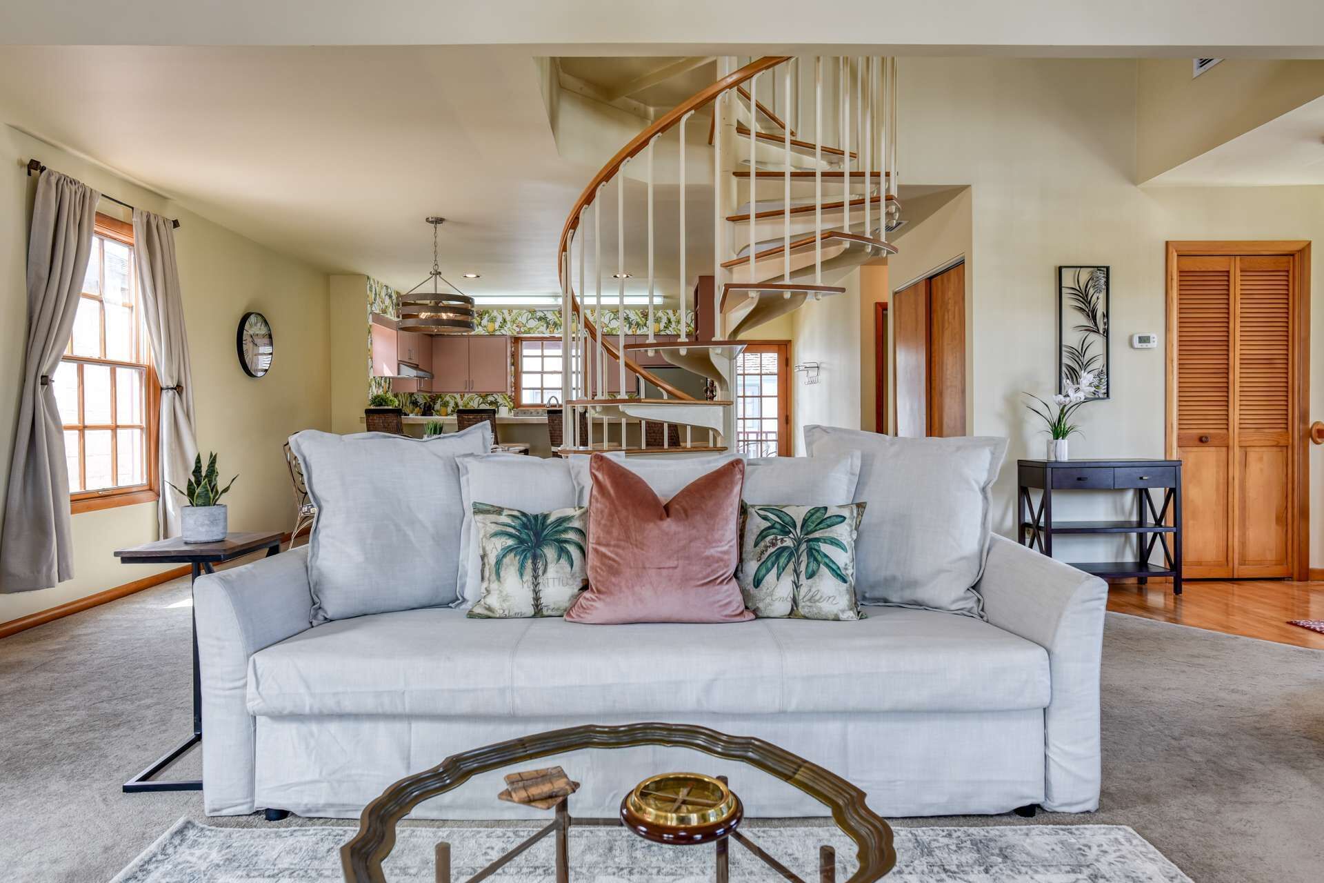 A spacious living room with a white sofa, a wooden coffee table, and a spiral staircase.