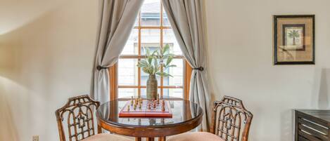A dining area with a round table, two chairs, a vase with a plant, and a framed picture on the wall.