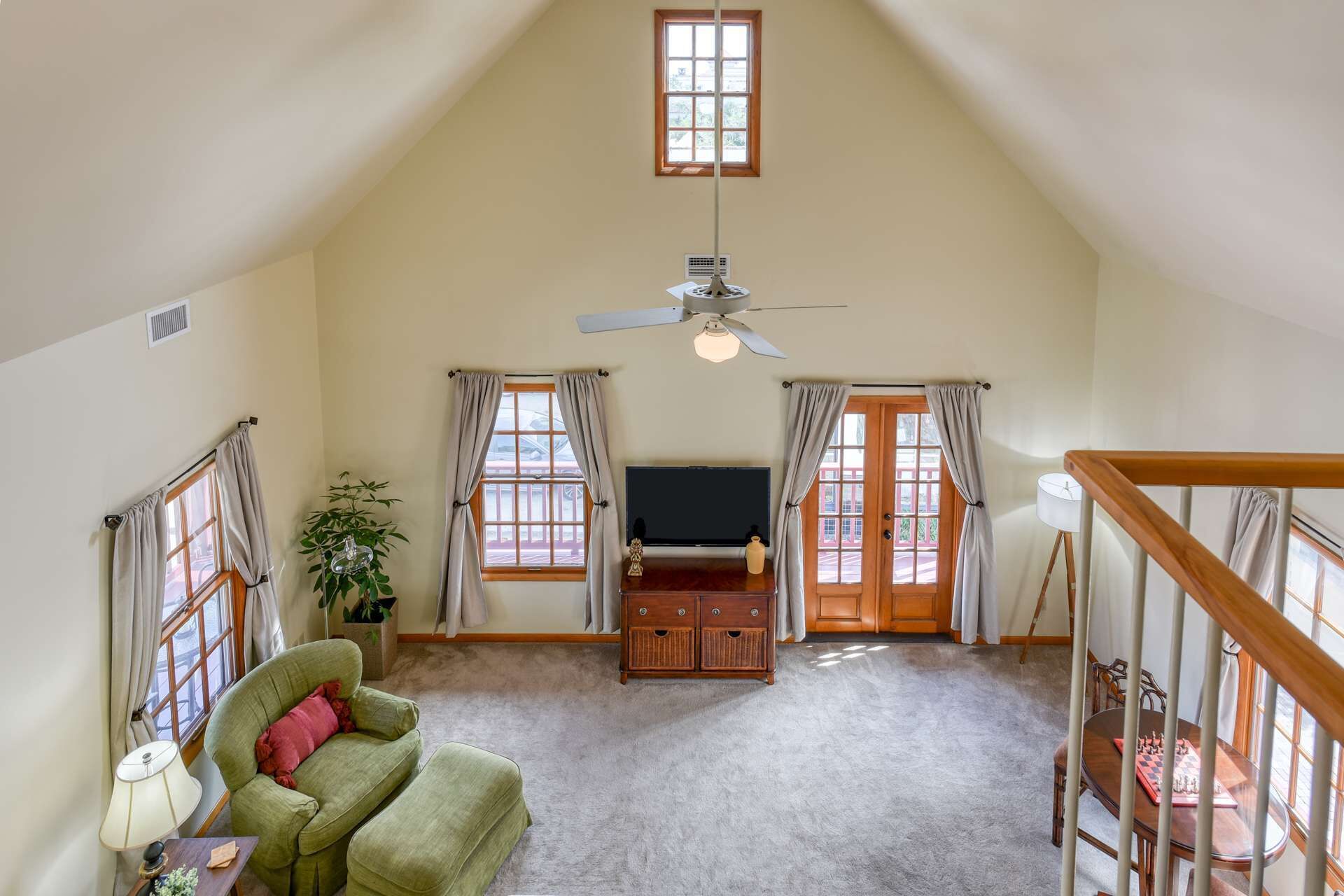 Een ruime loft met een hoge plafond, een plafondventilator en een groot raam met gordijnen.