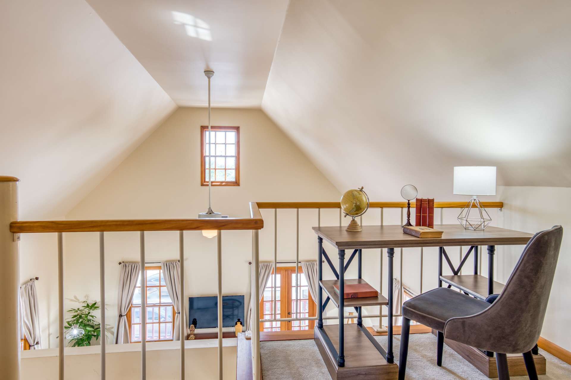 A loft-style bedroom with a wooden ceiling, a desk with a globe and books, a chair, and a window with curtains.