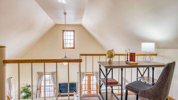 A loft-style bedroom with a wooden ceiling, a desk with a globe and books, a chair, and a window with curtains.