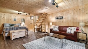 A wooden cabin interior with a bed, a sofa, a coffee table, a staircase, and a framed picture on the wall. - Book Your 2026 Vacation!, Private!, Hot Tub, Great for Families, Sleeps 8! (Sevierville)