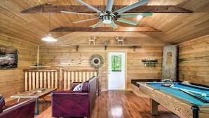 A wooden cabin interior with a pool table, a red sofa, and a ceiling fan. - Book Your 2026 Vacation!, Private!, Hot Tub, Great for Families, Sleeps 8! (Sevierville)