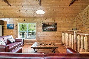 Relax in this cabin-style room with a wooden ceiling, exposed beams, and a large window offering a view of the surrounding greenery.