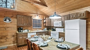 A wooden cabin-style kitchen with a dining table set for four, wooden cabinets, a refrigerator, and a coffee maker. - Book Your 2026 Vacation!, Private!, Hot Tub, Great for Families, Sleeps 8! (Sevierville)