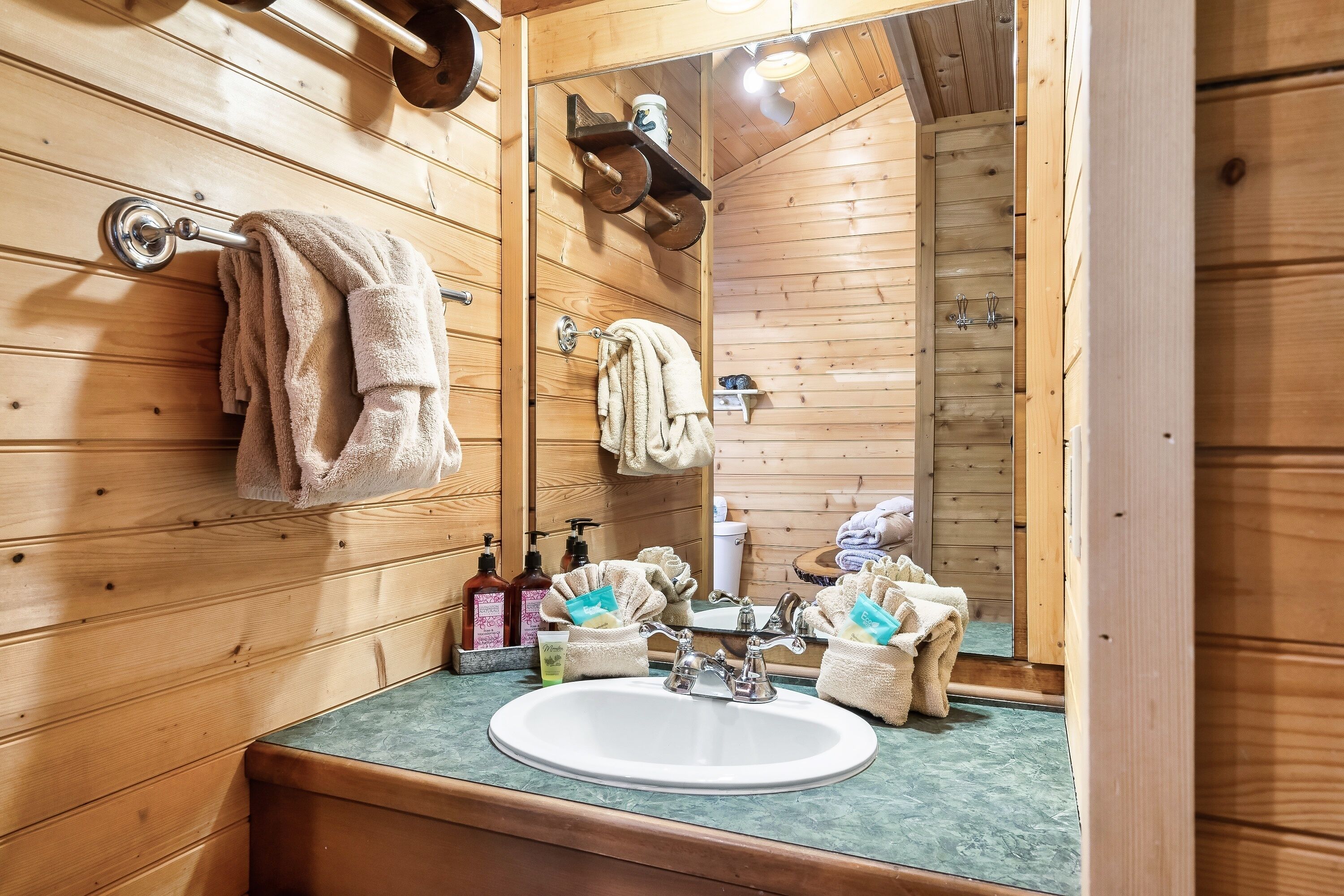 A wooden cabin bathroom with a sink, towel rack, and toiletries.