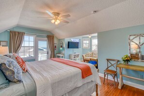 Une chambre à coucher comprenant un lit, un bureau, une chaise, un ventilateur de plafond et un téléviseur.