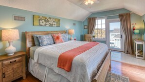 Une chambre à coucher comprenant un lit, deux tables de chevet, un ventilateur de plafond, une fenêtre avec des rideaux et une vue sur l’extérieur.
