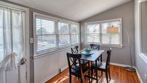 A dining area with a table and chairs, large windows with blinds, a floor lamp, and a radiator. - Seaside Cottage (St. Augustine)