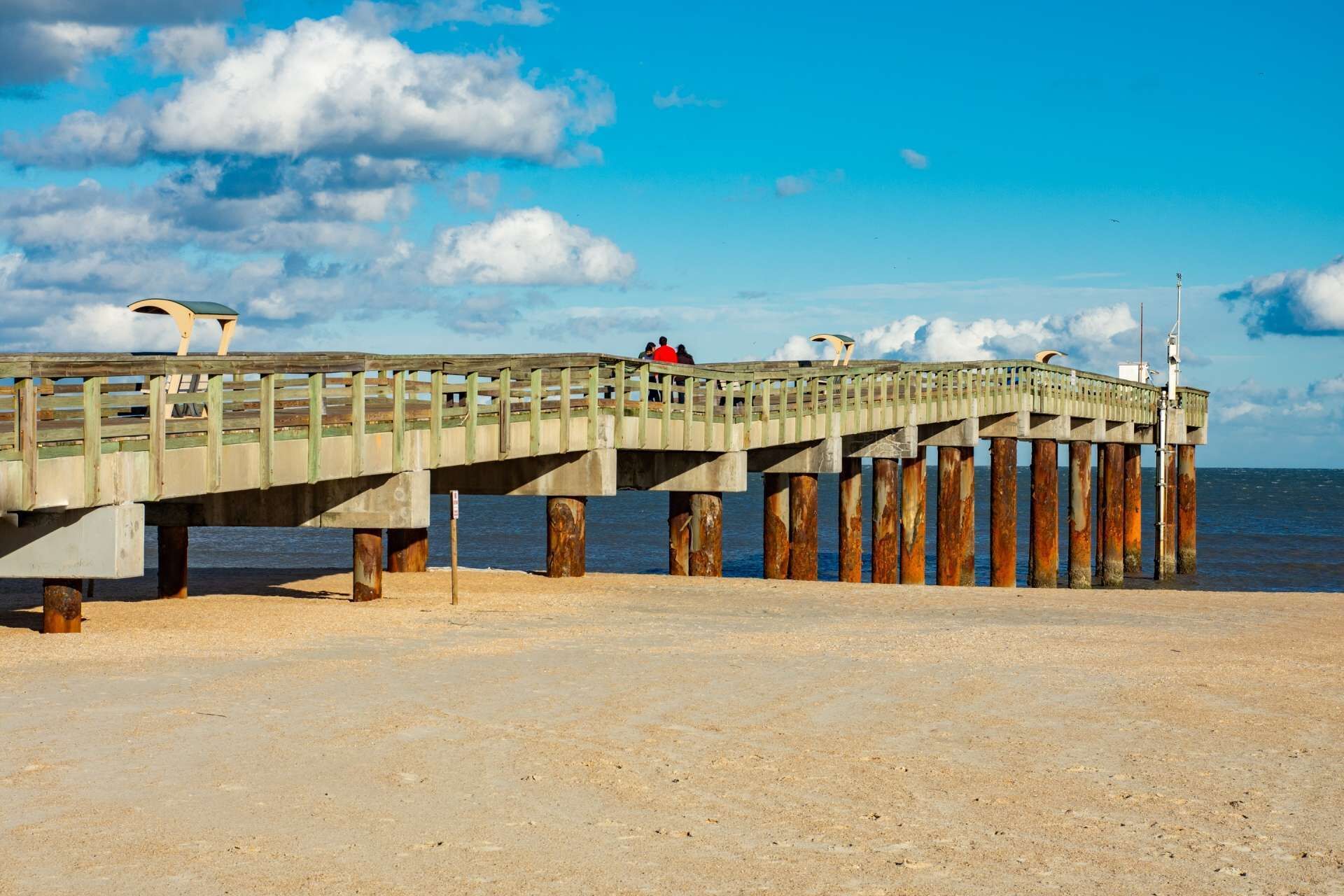 A wooden pier extending into the water with a metal railing, supported by rusted pilings.