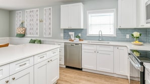 Una cocina moderna con alacenas blancas, lavavajillas, pileta y estufa.