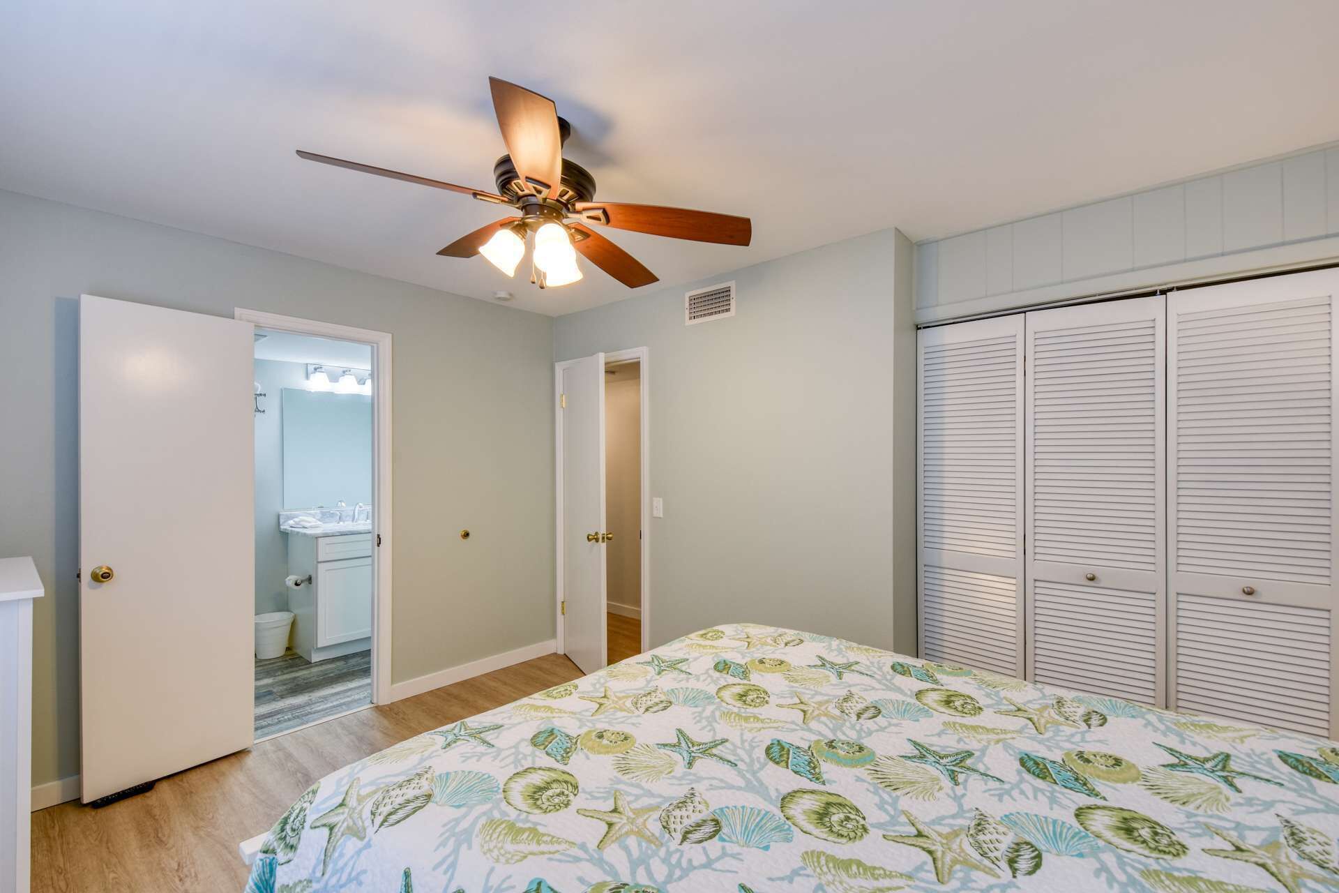 A bedroom with a bed, a ceiling fan, a walk-in closet, and a bathroom visible through an open door.