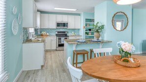 Cocina con gabinetes blancos, microondas y estufa. Hay un comedor con mesa y sillas de madera.