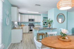 Cocina con gabinetes blancos, microondas y estufa. Hay un comedor con mesa y sillas de madera.