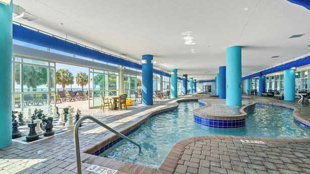 An indoor swimming pool with blue pillars, a tiled deck, and lounge chairs. - Bay View Resort by Elliott Beach Rentals (Myrtle Beach)