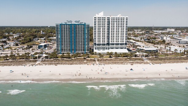 A coastal cityscape with two prominent high-rise buildings, a sandy beach, and a clear blue sky. - Bay View Resort by Elliott Beach Rentals (Myrtle Beach)