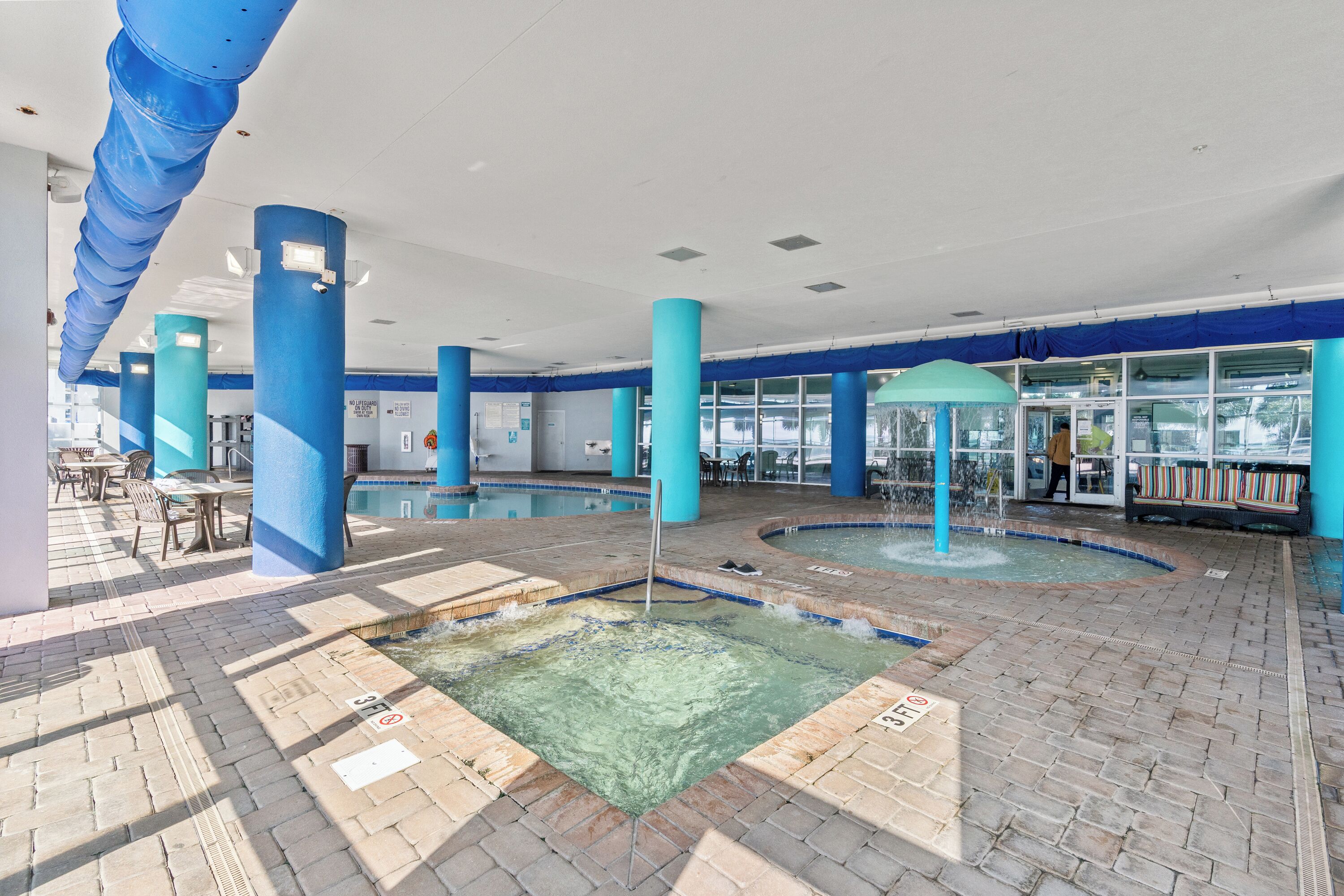 Un espace piscine agrémenté de piliers bleus, d’un sol carrelé et d’une enceinte en verre.