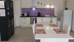 A modern kitchen with white cabinets, a purple backsplash, and a dining area with a white table and chairs. - 2 Bedroom Apartment in Anduze (Anduze)