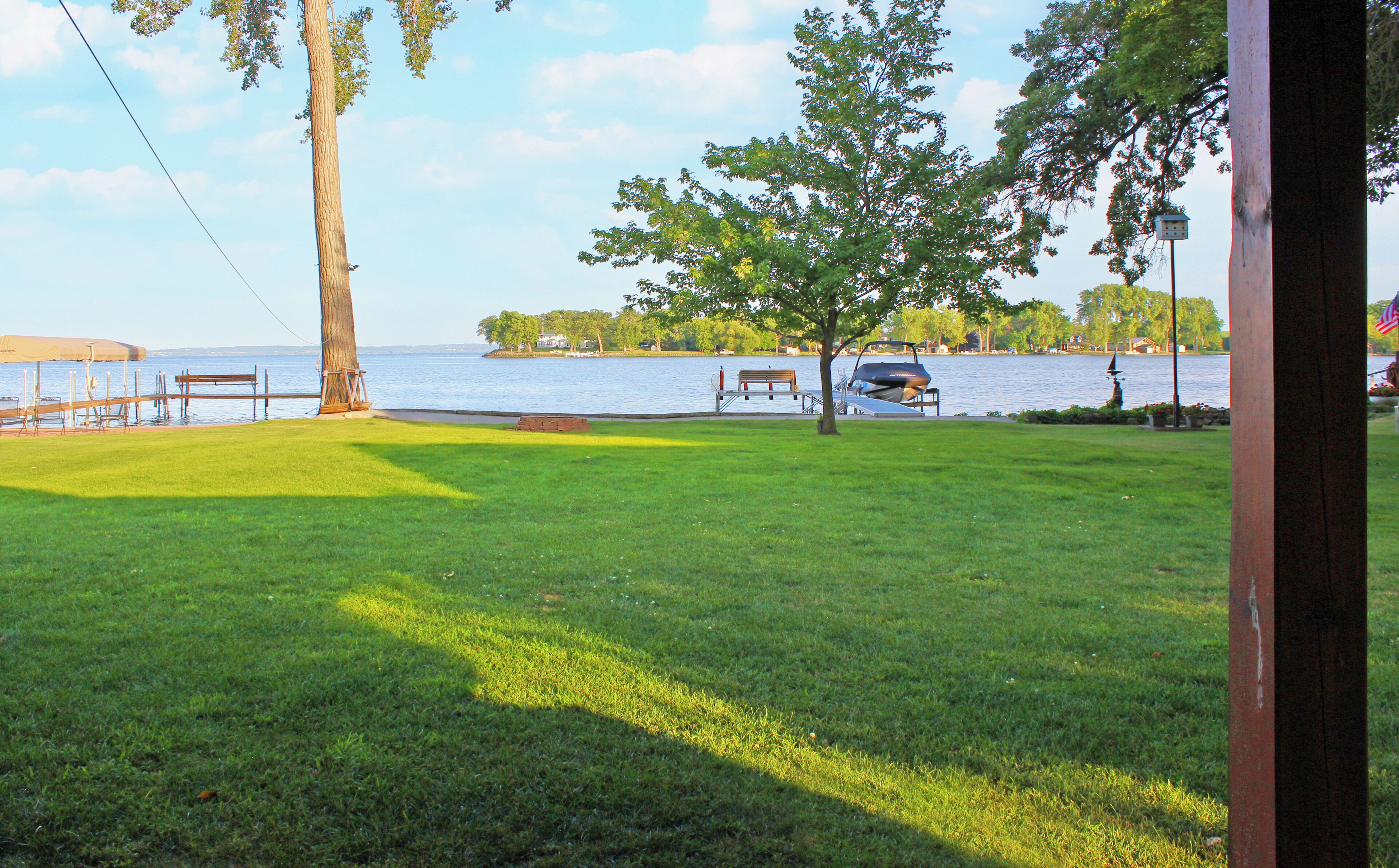 A grassy area with a bench and a tree, overlooking a body of water with a dock and a boat.