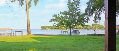 A grassy area with a bench and a tree, overlooking a body of water with a dock and a boat.