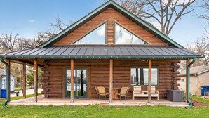 Une cabane en rondins dotée d’un porche couvert, de grandes fenêtres et d’un toit en métal.