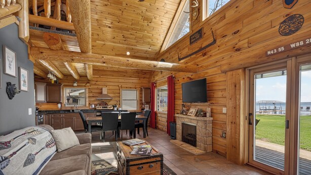 L’intérieur d’une cabane en rondins comprend un coin repas, une cuisine, une cheminée et une grande fenêtre donnant sur un quai.
