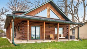Une cabane en rondins dotée d’un porche couvert, de grandes portes-fenêtres coulissantes et d’un petit espace de détente extérieur.