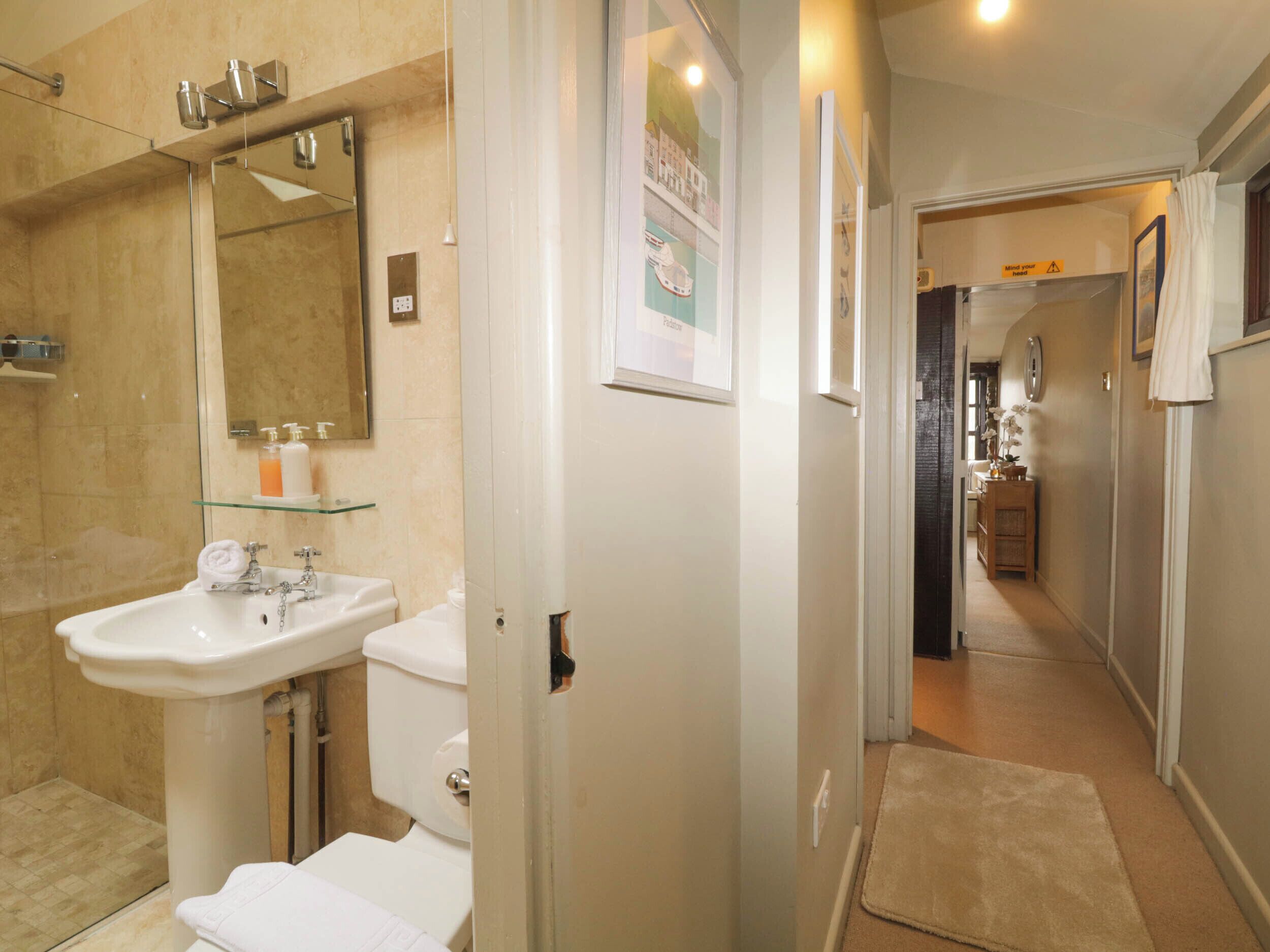 Ein modernes Badezimmer mit einer Duschkabine aus Glas, einem weißen Waschbecken und einer Toilette. Über dem Waschbecken hängt ein Spiegel und an der Wand hängt ein gerahmtes Bild.