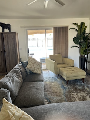 A living room with a gray sectional sofa, a beige armchair, and a coffee table. There is a wooden cabinet and a large potted plant.