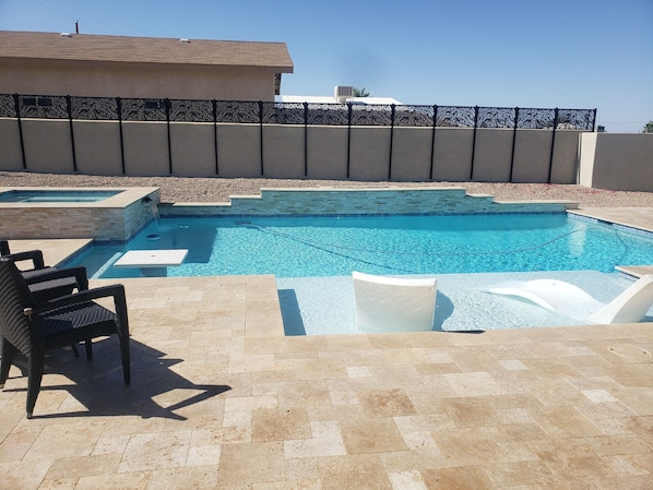 A swimming pool with a tiled deck, a lounge chair, and a stone wall.
