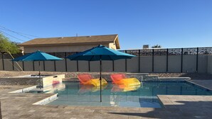 Une piscine avec trois toboggans gonflables, une terrasse en briques et deux parasols bleus.