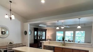 A kitchen with a central island, wooden cabinets, a dining area with a table and chairs, pendant lighting, and a view of the outdoors through windows. - Cozy 3-Bedroom Home in North Port (North Port)