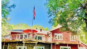 A two-story house with a balcony, a stone foundation, and a red exterior. - The Good Place: Lakehouse Near Dunbar ATV Trails/On Blue Ox Trails (Fence)