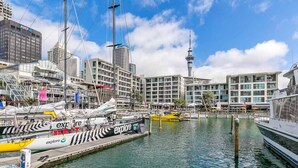 A marina with boats docked, a prominent tower in the background, and modern buildings. - Penthouse Glory - Sebel (Auckland)