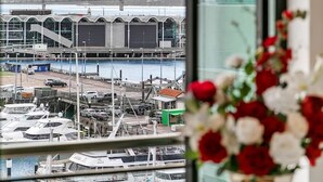 A view of a marina with boats docked, a bridge in the background, and a building with a large garage door. - Penthouse Glory - Sebel (Auckland)