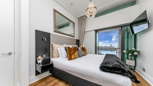 A modern bedroom with a bed, bedside table, mirror, and a view of a body of water. - Penthouse Glory - Sebel (Auckland)