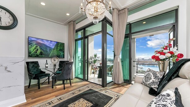 A modern living room with a television, a chandelier, a sofa, and a view of the city. - Penthouse Glory - Sebel (Auckland)