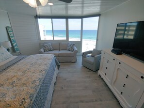 A bedroom with a bed, a sofa, a TV, and a view of the beach.