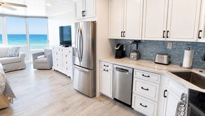 Una cocina moderna con gabinetes blancos, electrodomésticos de acero inoxidable y vista al océano.