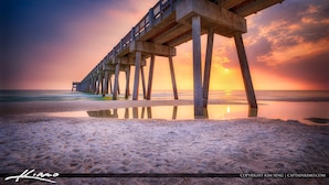 Un muelle se adentra en el océano con un atardecer de fondo.