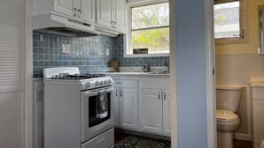 Une cuisine de taille réduite avec des meubles blancs, une cuisinière à gaz et une fenêtre au-dessus de l’évier.